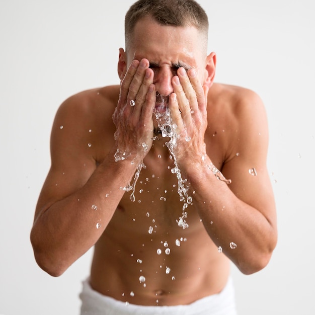 Foto vista frontal del hombre sin camisa lavándose la cara