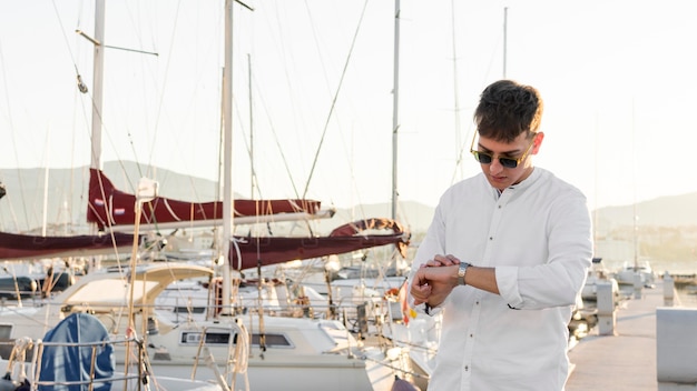 Foto vista frontal del hombre con gafas de sol en el puerto deportivo mirando el reloj