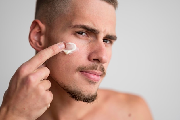 Foto vista frontal del hombre guapo aplicando crema facial