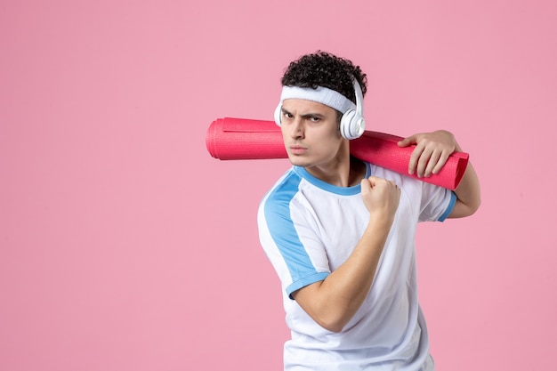 Vista frontal del hombre joven confiado en ropa deportiva con estera de yoga