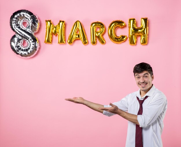 Vista frontal hombre joven con decoración de marzo sobre fondo rosa presente igualdad femenina día de la mujer matrimonio hombre color