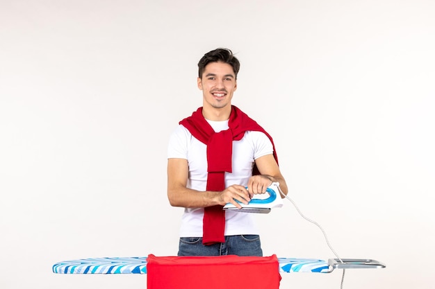 Vista frontal del hombre joven detrás de la tabla de planchar sobre fondo blanco, trabajo de lavandería, hombre emoción, hogar, limpieza, tareas domésticas