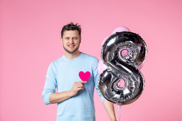 Vista frontal hombre joven con lindos globos y pegatina de corazón sobre fondo rosa amor día de la mujer matrimonio igualdad fecha marzo sensual femenino divertido