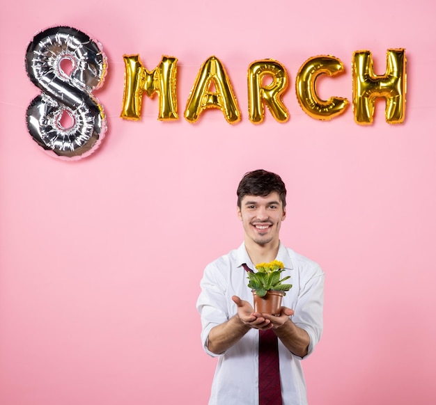 Vista frontal hombre joven con pequeña flor y decoración de marzo sobre fondo rosa colores de hombre presente fiesta del día de la mujer matrimonio femenino igualdad