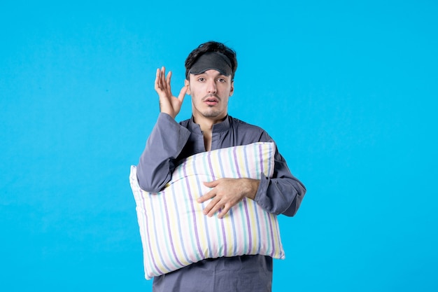 Vista frontal hombre joven en pijama y vendaje para dormir sosteniendo la almohada sobre fondo azul color pesadilla tardía noche humana descanso despierto sueño sueño