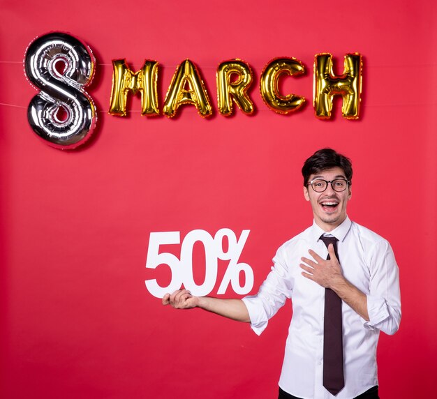 Foto vista frontal hombre joven sosteniendo la escritura sobre fondo rojo mujer color sensual fiesta día de la mujer marzo presente moda compras