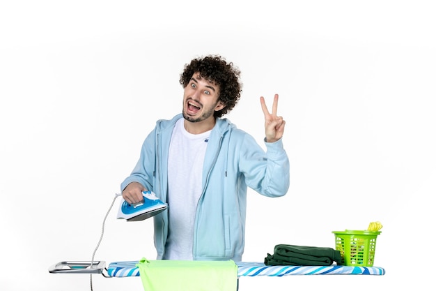 Vista frontal del hombre joven sosteniendo hierro sobre fondo blanco color de planchado hombre lavandería ropa quehaceres domésticos limpieza emoción