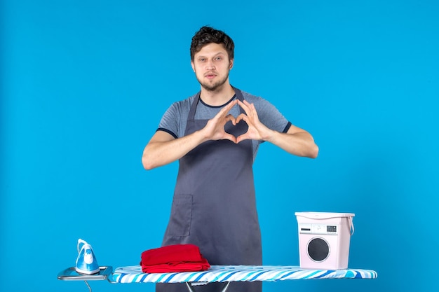 Vista frontal del hombre joven con tabla de planchar sobre fondo azul hombre ropa quehaceres domésticos lavadora limpieza plancha colores de lavandería