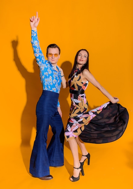 Vista frontal del hombre y la mujer vestidos con ropa como de los años 70 en la pared amarilla aislada | Foto Premium Vista frontal del hombre y la mujer vestidos con ropa como de los años 70 en la pared amarilla aislada | Foto Premium
