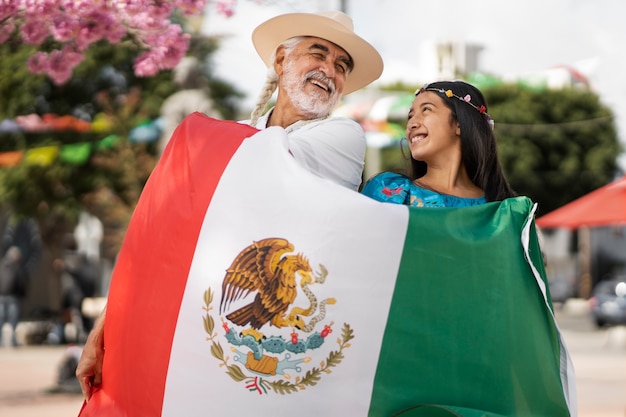 Foto vista frontal hombre y niña con bandera mexicana