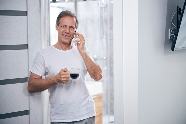 Vista frontal de un hombre satisfecho con una taza de café llamando por teléfono