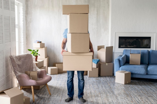 Vista frontal del hombre sujetando cajas mientras se muda cubriéndose la cara