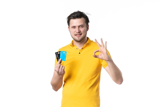 Vista frontal de los hombres jóvenes en camisa amarilla sosteniendo un par de tarjetas bancarias sobre fondo blanco trabajo uniforme gastar dinero color humano