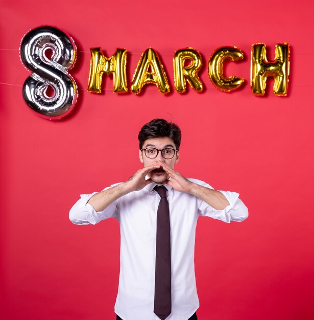 Vista frontal de los hombres jóvenes con decoración de marzo sobre fondo rojo, presente de vacaciones, color de moda, regalo del día de la mujer, mujer de pasión