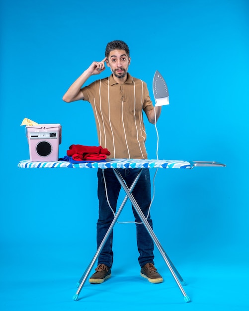 Vista frontal de los hombres jóvenes detrás de la tabla de planchar sobre fondo azul color de las tareas del hogar máquina de lavandería limpia lavado emoción hombre