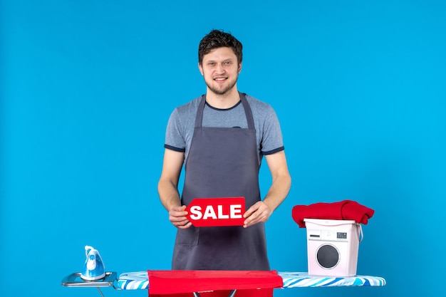 Vista frontal de los hombres jóvenes con venta roja escribiendo en sus manos sobre fondo azul plancha de compras lavadora quehaceres domésticos lavandería