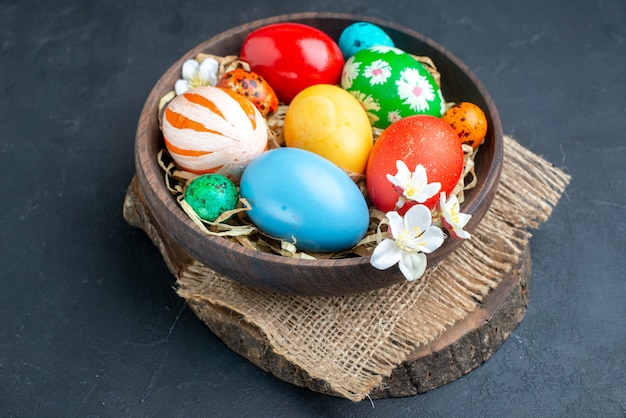 Vista frontal de los huevos de pascua de color dentro de la placa con paja en la superficie oscura ornamentados coloridos colores de primavera de vacaciones grupo multi concepto