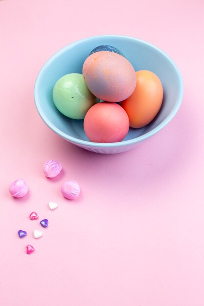 Vista frontal de los huevos de pascua de color dentro de la placa en la superficie rosada vacaciones ornamentadas Pascua colorido étnico multi colores primavera