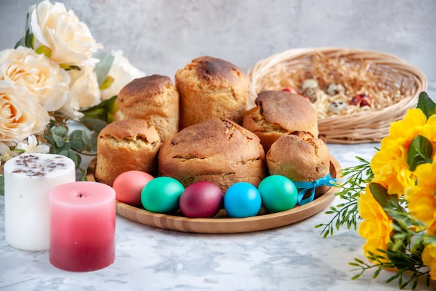 Vista frontal de los huevos de pascua de color con pan de vacaciones y tortas dentro de la bandeja sobre fondo blanco dulce concepto colorido pastel ornamental