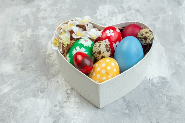 Vista frontal de los huevos de pascua de colores dentro de la caja en forma de corazón sobre fondo blanco concepto de feminidad de pascua ornamentado primavera colorido de novruz