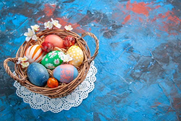 Vista frontal de los huevos de pascua de colores dentro de la canasta sobre la superficie azul