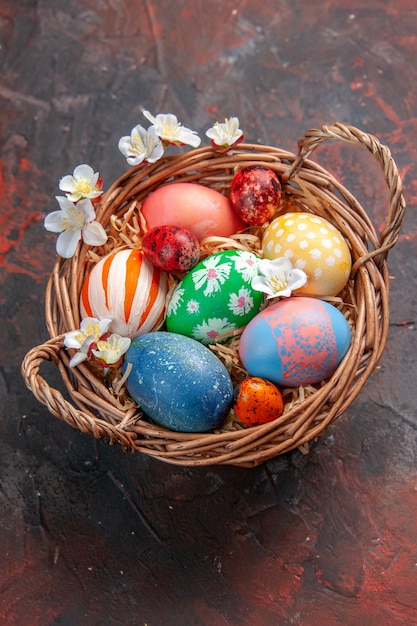 Vista frontal de los huevos de Pascua de colores dentro de la canasta sobre una superficie oscura