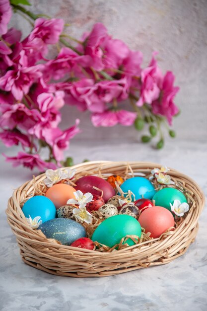 Vista frontal de los huevos de pascua de colores dentro de la cesta sobre la superficie blanca primavera colorida vacaciones concepto de pascua