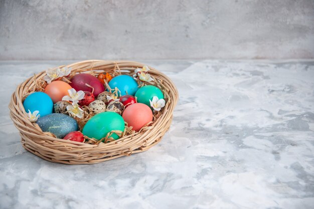 Vista frontal de los huevos de pascua de colores dentro de la cesta sobre la superficie blanca primavera colorido concepto de pascua ornamentado