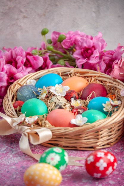 Vista frontal de los huevos de pascua de colores dentro de la cesta en la superficie rosada primavera de pascua colorido concepto de vacaciones de colores ornamentados