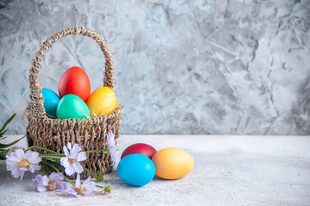 Vista frontal de los huevos de pascua de colores dentro de una hermosa canasta sobre una superficie blanca