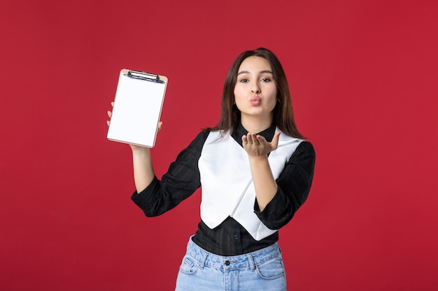 vista frontal jovem bonita garçonete de uniforme segurando nota de arquivo para pedidos em fundo vermelho trabalho beleza mulher jantar noite trabalho beijo comida