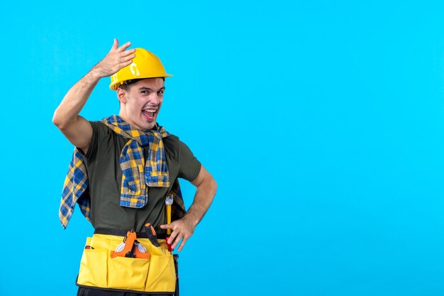 vista frontal jovem construtor masculino com capacete amarelo no fundo azul plana trabalhador construtor arquitetura construção de ferramentas de cores