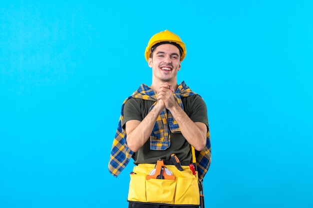 vista frontal jovem construtor masculino em capacete amarelo na cor de fundo azul plana construtor arquitetura ferramenta edifícios trabalhador