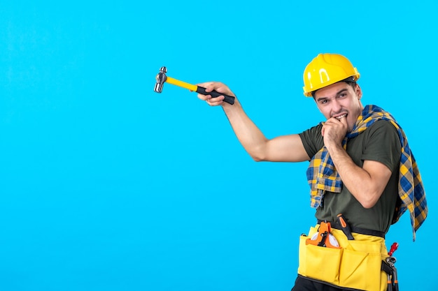 vista frontal jovem construtor masculino segurando o martelo no fundo azul casa trabalho prédio trabalhador arquitetura construtor