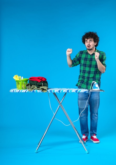 vista frontal jovem do sexo masculino com tábua de engomar sobre fundo azul máquina de lavar roupa humana de casa cor limpa