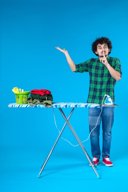 vista frontal jovem do sexo masculino com tábua de passar roupa pedindo para ficar em silêncio sobre fundo azul máquina de lavar roupa trabalho doméstico roupas limpas humanas