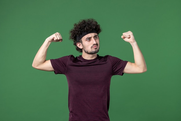 vista frontal jovem do sexo masculino flexionando em um fundo verde cor esporte ginásio treino atleta correndo modelo de saúde emoção