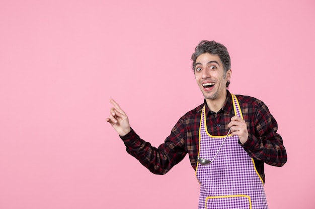 vista frontal jovem do sexo masculino na capa segurando uma colher de sopa e interagindo com alguém no fundo rosa cozinheiro cozinha cozinha comida profissão marido trabalhador horizontal