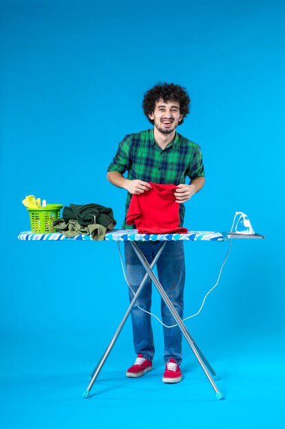 vista frontal jovem do sexo masculino segurando a camisa no fundo azul limpo máquina de lavar roupa trabalho doméstico cor humana