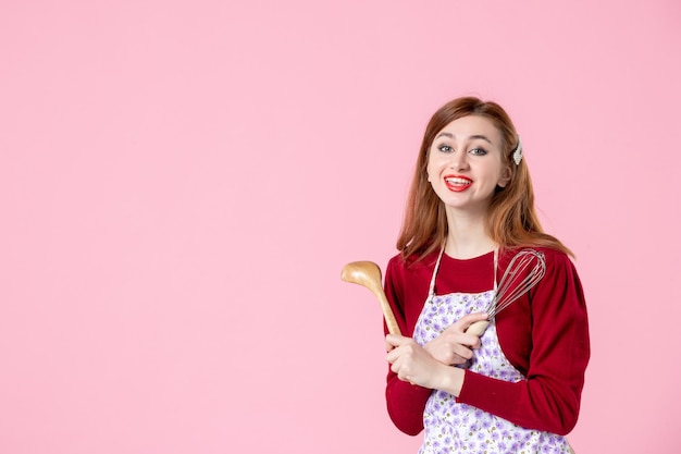 vista frontal jovem dona de casa com colher e bata na cor de fundo rosa cozinhar torta cozinha massa doce comida mulher bolo