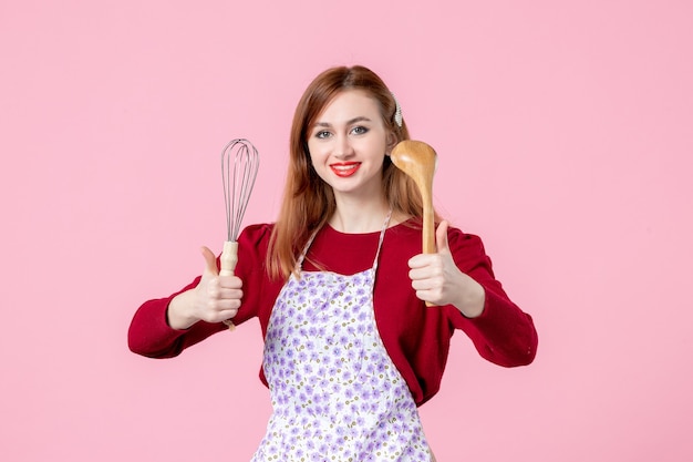 Vista frontal jovem dona de casa posando com batedor e colher de pau no fundo rosa bolo profissão cozinhar massa cozinha mulher torta horizontal