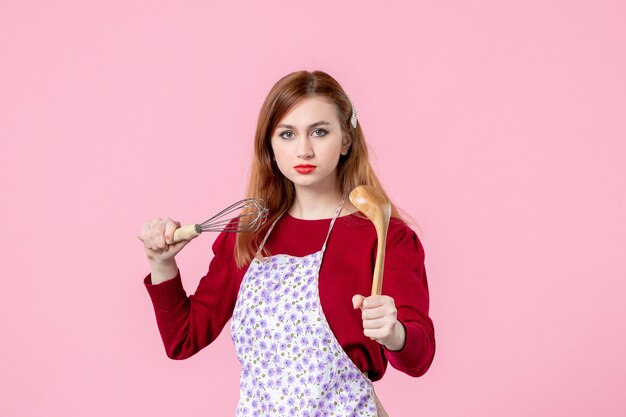 vista frontal jovem dona de casa posando com batedor e colher de pau no fundo rosa profissão cozinhar massa torta mulher cozinha uniforme horizontal