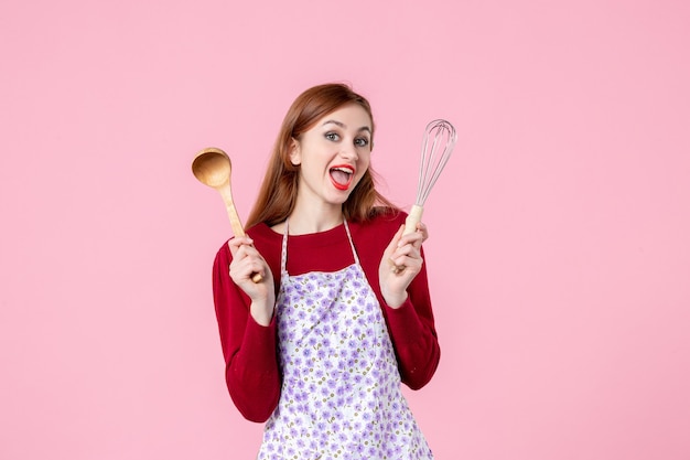 vista frontal jovem dona de casa segurando um batedor e uma colher de pau no fundo rosa massa bolo cozinha horizontal uniforme mulher cozinhar profissão de torta