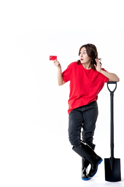 Foto vista frontal jovem fêmea segurando uma pá preta e um cartão do banco no fundo branco mulher trabalho solo cavando trabalho solo noite cores dinheiro