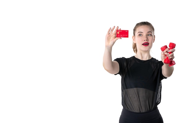 vista frontal jovem feminino com halteres e cartão do banco nas mãos no fundo branco ginásio dinheiro corpo atleta estilo de vida saúde