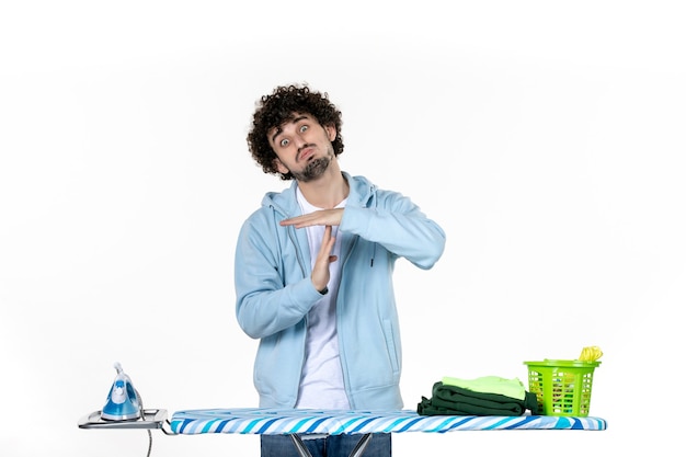 vista frontal jovem homem atrás de tábua de passar roupa no fundo branco roupas foto do homem limpeza ferro trabalho doméstico roupa a cores