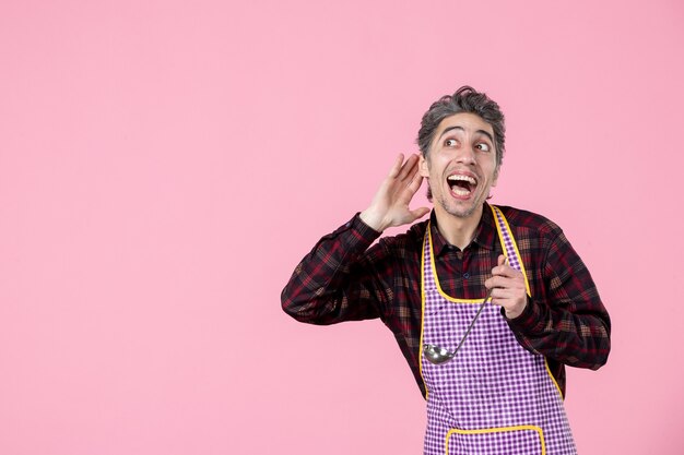 vista frontal jovem homem na capa segurando colher de sopa e interagindo fundo rosa trabalho profissão horizontal cozinha cozinheiro trabalhador comida marido