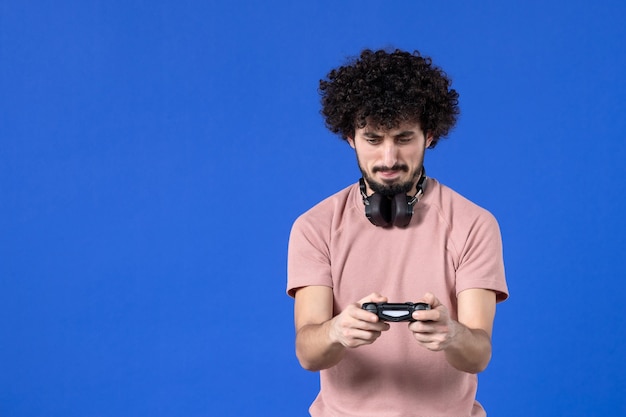 Foto vista frontal jovem jogando videogame com gamepad preto sobre fundo azul sofá virtual juvenil jogador de futebol adulto alegria adolescente