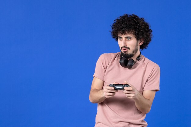 vista frontal jovem jogando videogame com gamepad preto sobre fundo azul sofá virtual juvenil jogador de futebol adulto ganhando alegria adolescentes