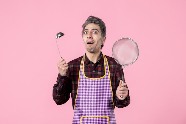 vista frontal jovem macho na capa com peneira e colher no fundo rosa cozinha trabalhador uniforme comida marido horizontal cozinheira de sopa